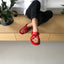 Person wearing red rope sandals sitting on a wooden bench with plants around.