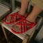 Red rope sandals worn by a person sitting on a wooden stool.