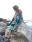 Person wearing a tie-dye dress sitting on rocks by the water