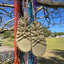 Pair of beige rope sandals with colorful straps hanging on a tree branch outdoors.