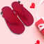 Red knitted slippers on a pink background with heart shapes and a gift box.