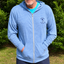 Man wearing a blue hoodie with a logo in front of green bushes